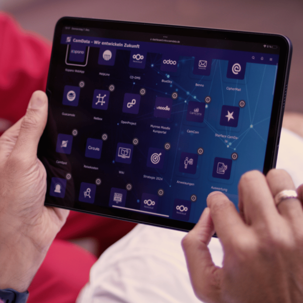 Person hält Tablet mit Dashboard voller App-Kacheln und Netzwerkvisualisierung, interagiert per Touch, modernes IT-Interface sichtbar.